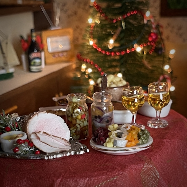 Jouluviikko. Kuvassa nukkekodin joulupäytä kinkkuineen ja tarjoiluineen. Taustalla joulukuusi.