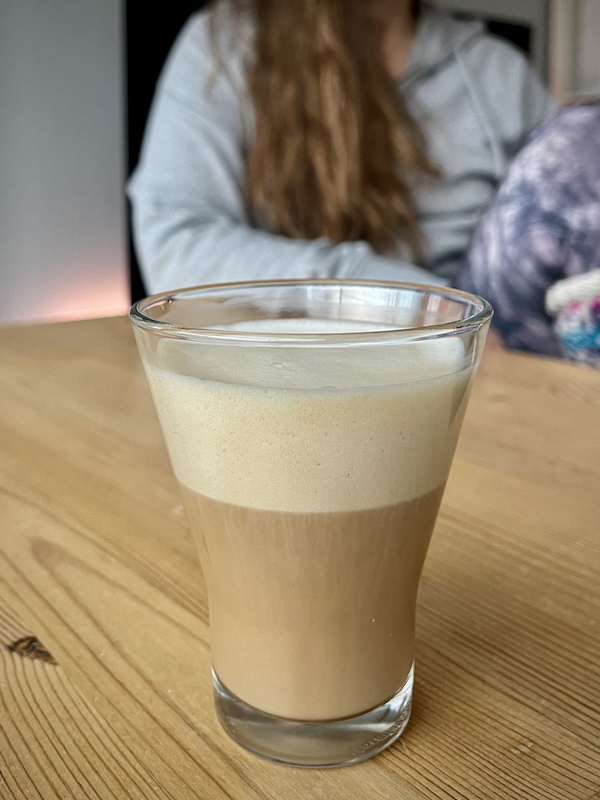 Joulukuun valoja ja varjoja. Kuvassa kahvia lasissa. Taustalla henkilö sumeampana.