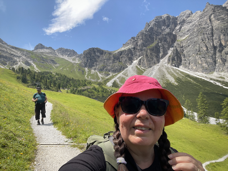Heinäkuun opit ja flopit. Kuvassa oma selfie, taustalla näkyy vuoria ja mies kävelemässä polulla.