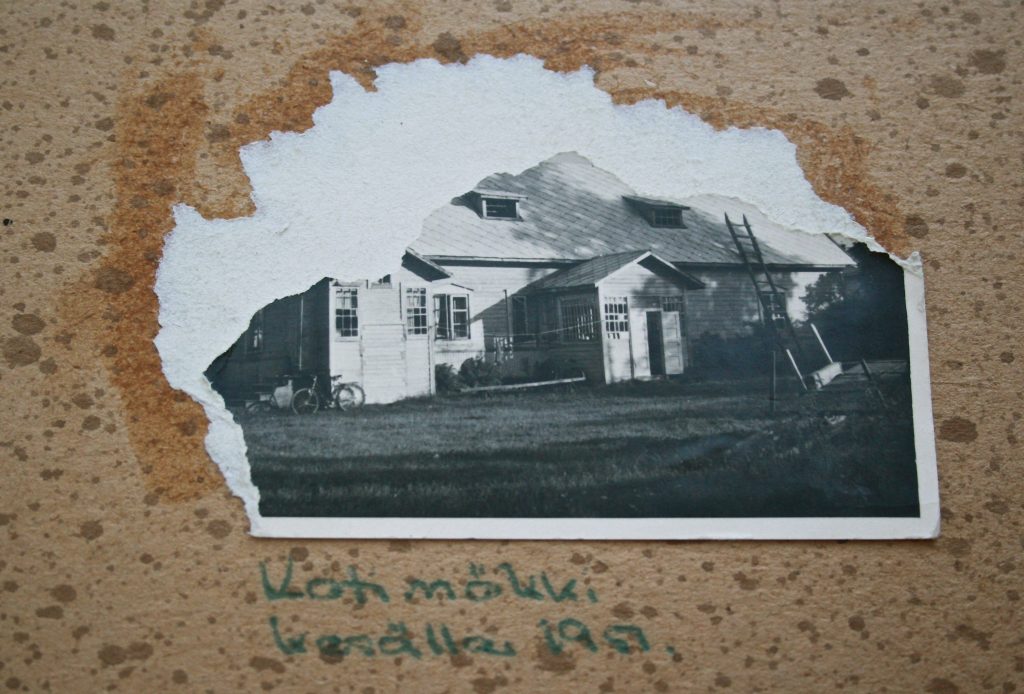 Juonekäänteitä ja kohtaloita. Kuvassa vanhasta valokuvakansiosta puiten vanhan talon valokuva. Valokuva on repäisty osittain rikki.